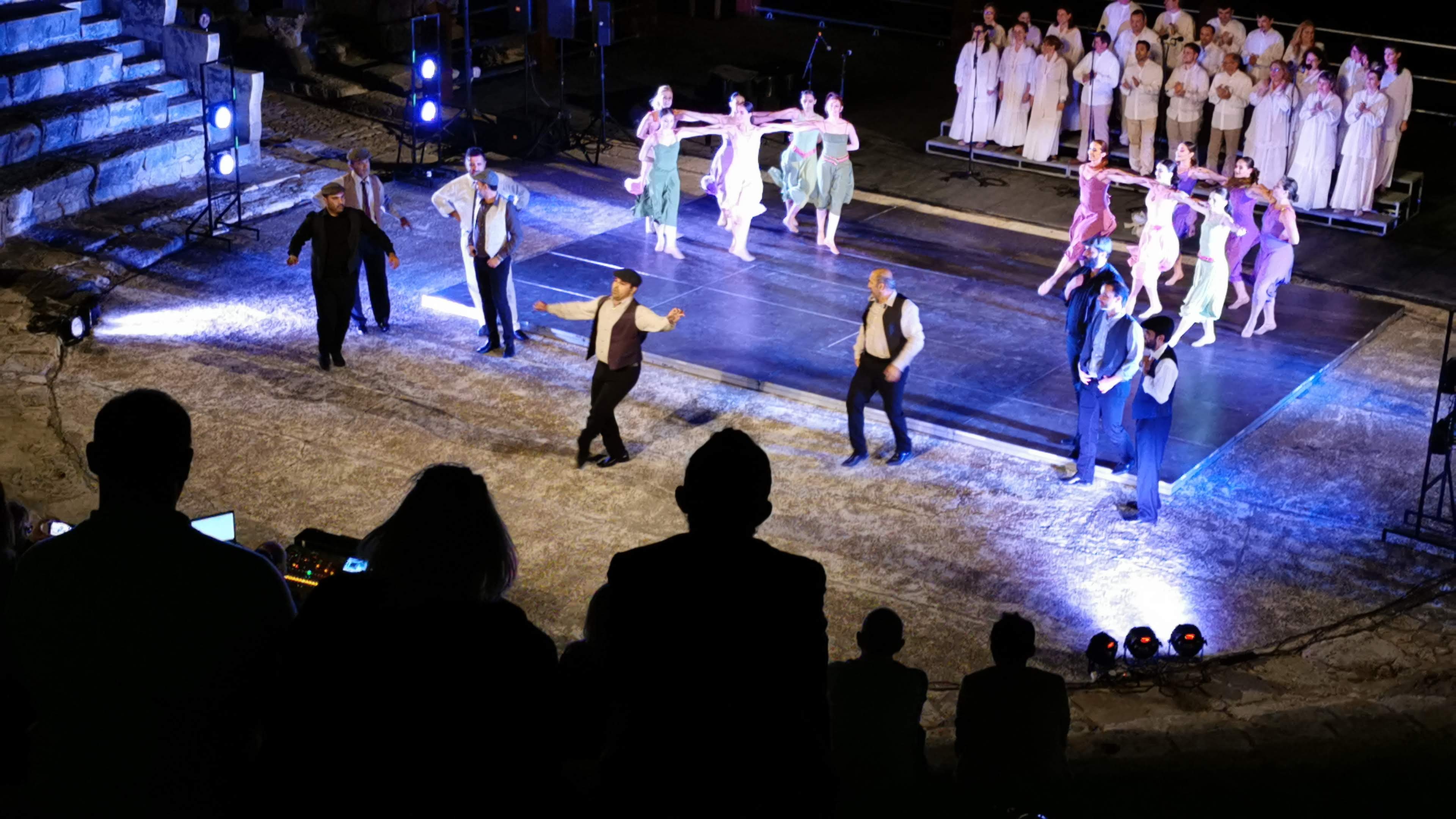 Ancient amphitheatre stage with performers and sea beyond at dusk