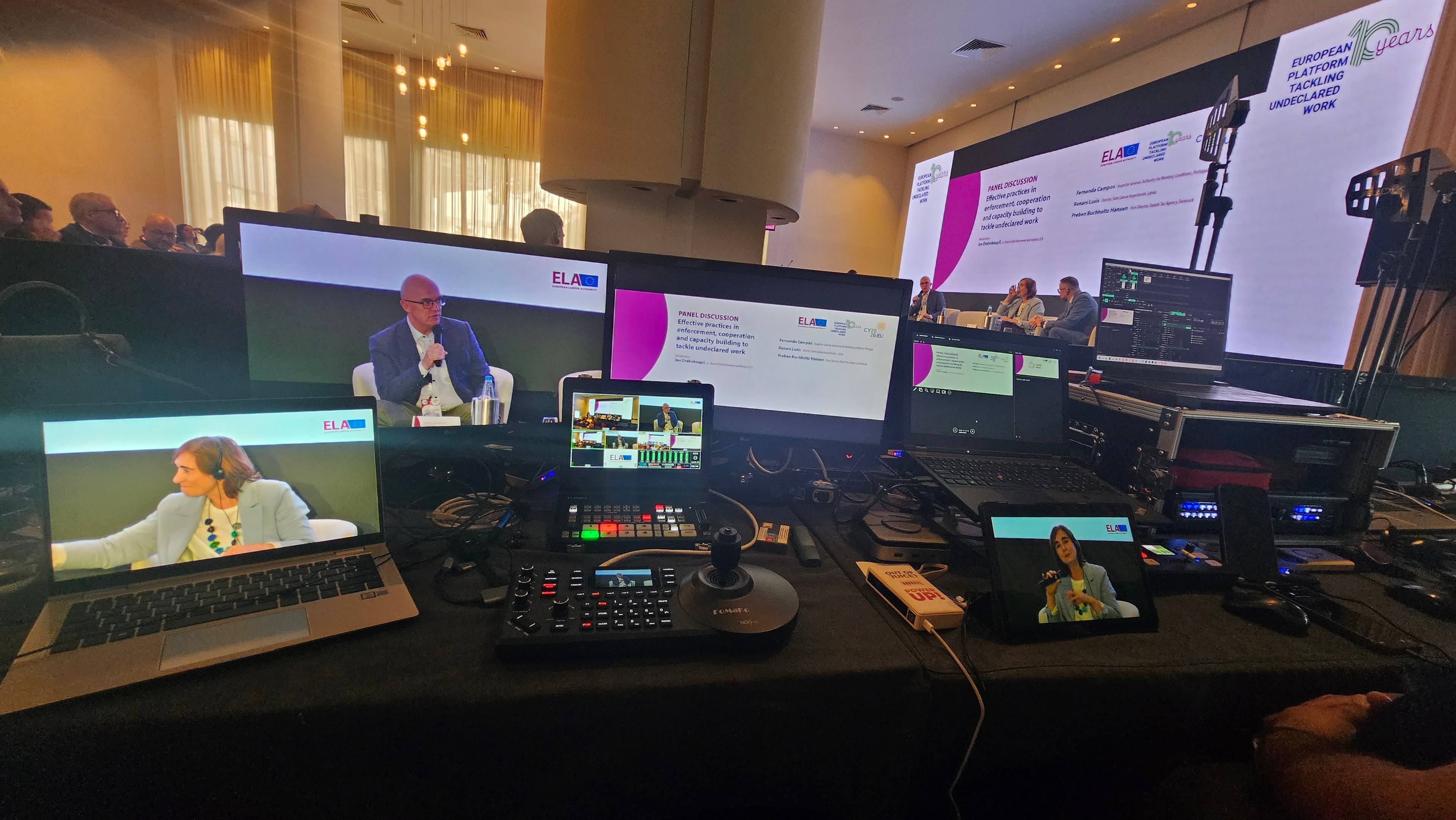 Broadcast production desk with screens showing a conference panel
